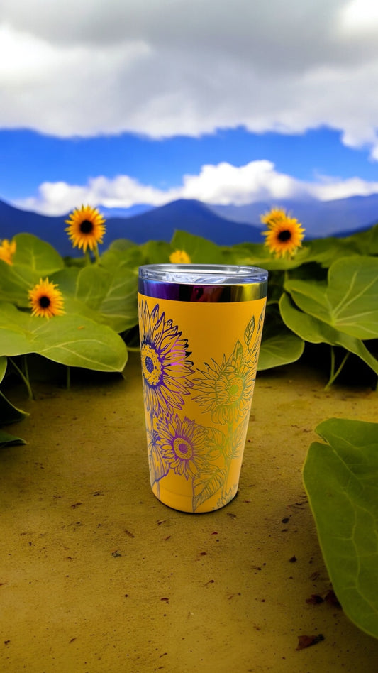 Yellow tumbler with floral design on a table with sunflowers and mountains in the background